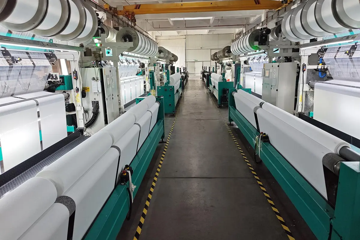 Rows of textile machines producing white fabric along a factory aisle