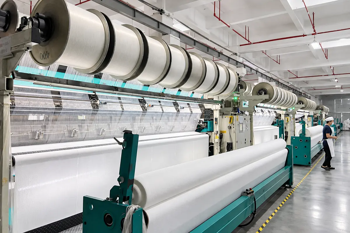Yarn beams feeding textile machines with wide rolls of white fabric