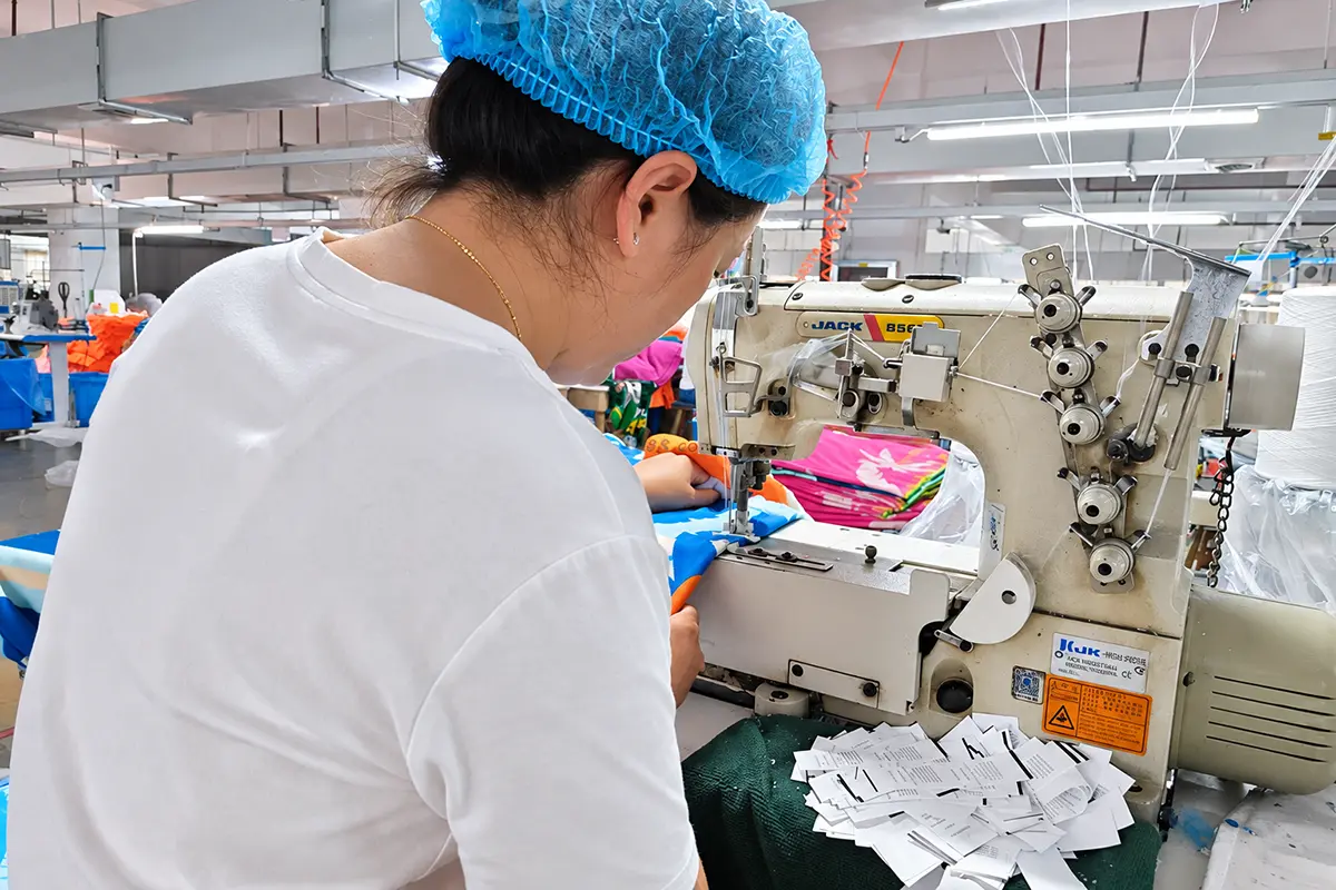 Worker sewing a printed towel beside a stack of care labels
