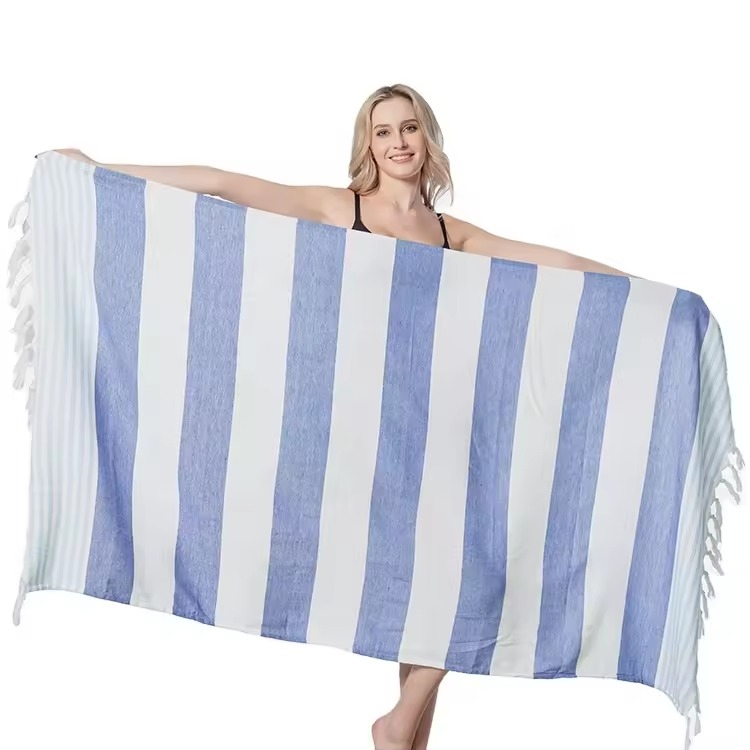 Blue and white striped Turkish beach towel with white fringe held open against a white background.