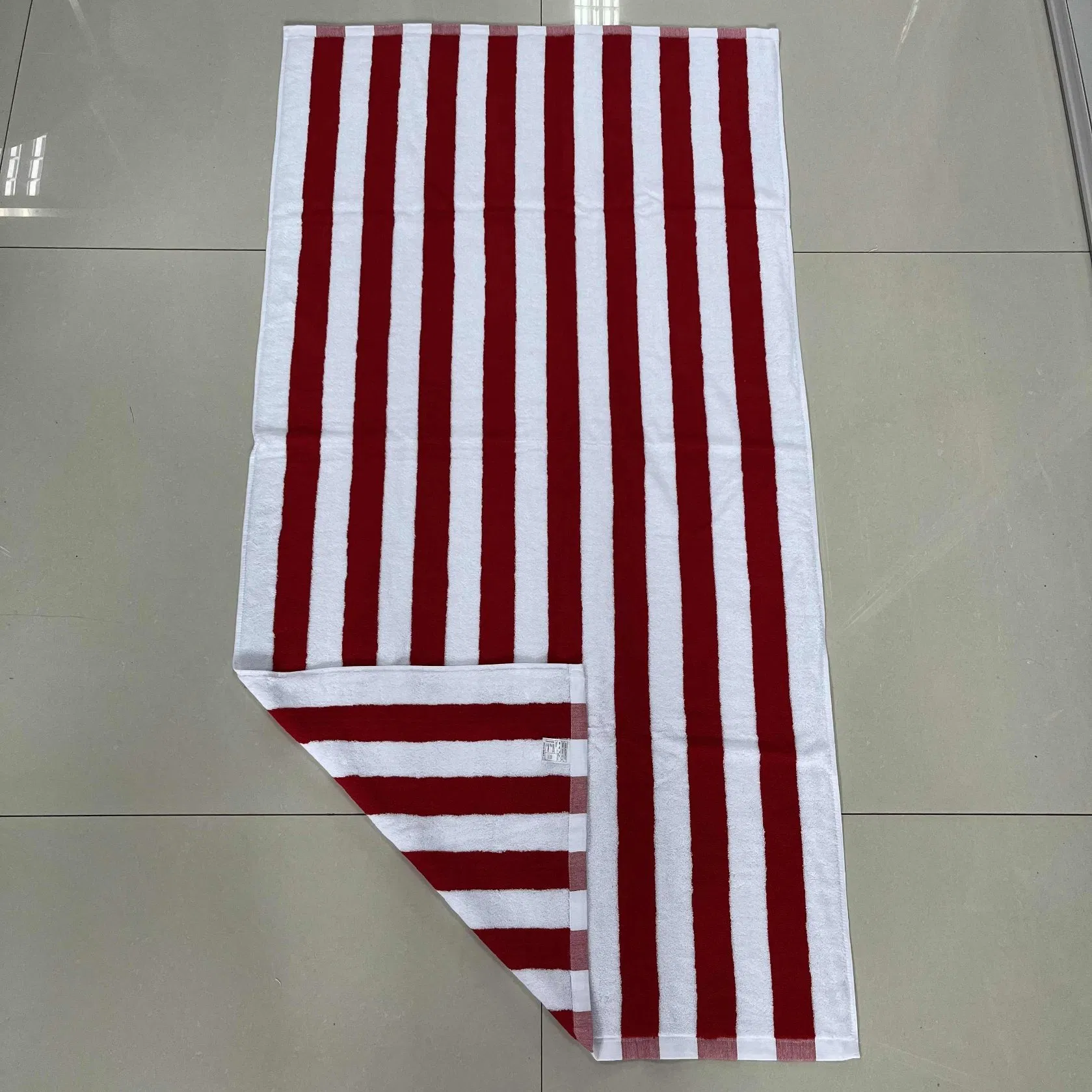 Red and white striped beach towel laid on a tiled floor with one corner folded back.