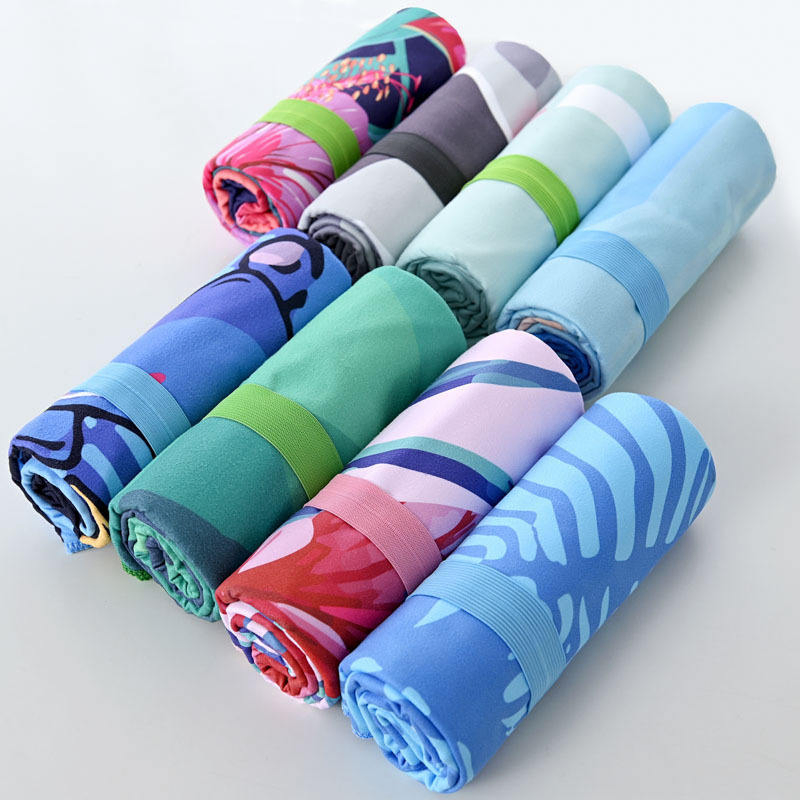 Rolled beach towels in assorted colors and prints secured with green, blue and pink elastic bands.