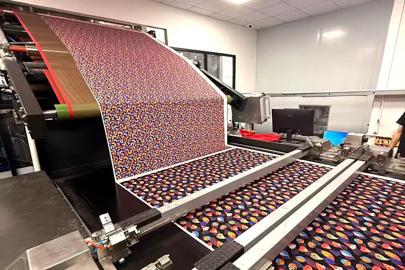 Colorful patterned textile rolls moving through printing production equipment.