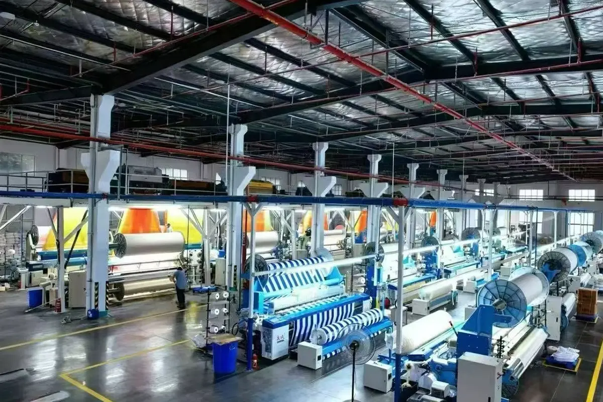 Rows of weaving machines producing white and blue-striped fabric on a factory production floor.