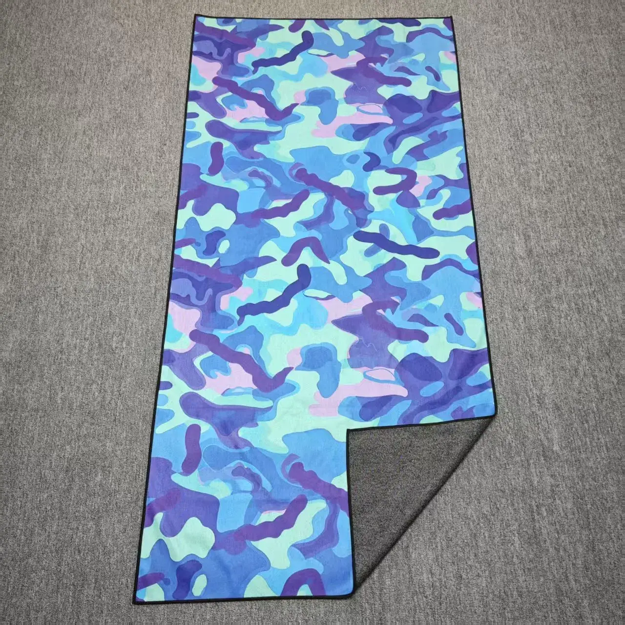 Blue, purple and mint camouflage beach towel with black edging and a folded corner showing its gray reverse.