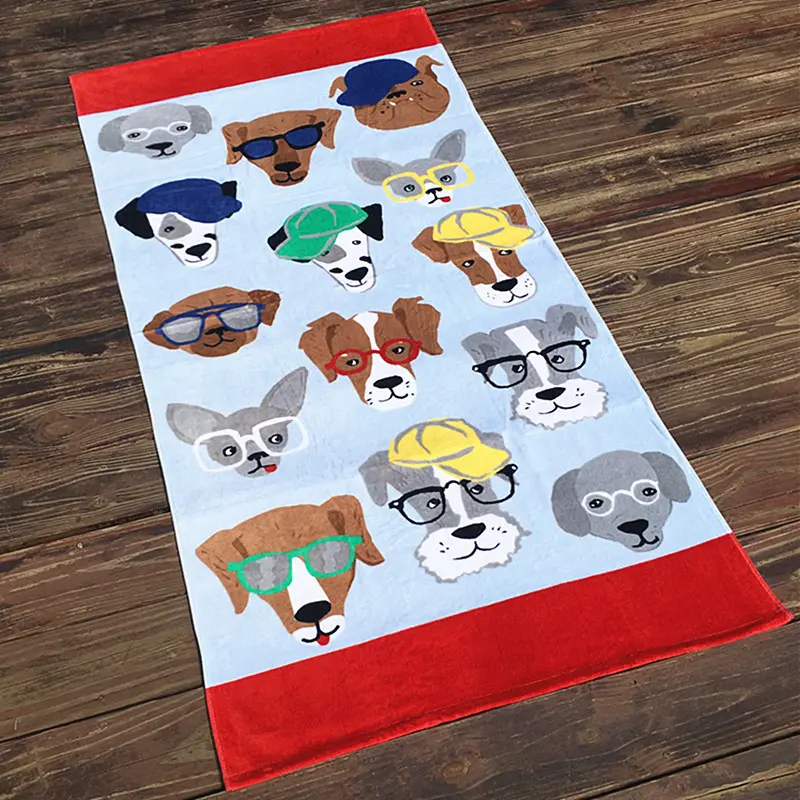 Pale blue beach towel with cartoon dog faces wearing glasses and caps and red end bands on a wooden floor.