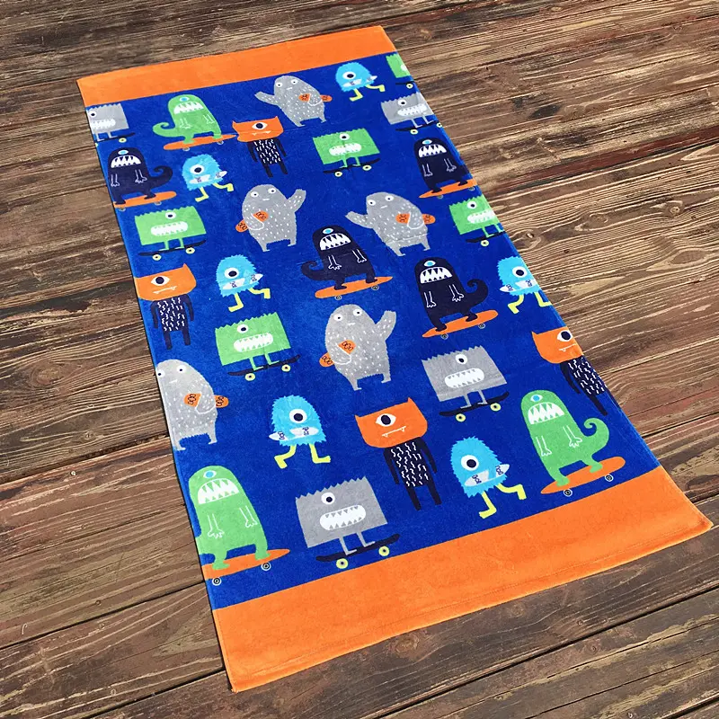 Blue beach towel with colorful cartoon monsters and orange end bands on a wooden floor.