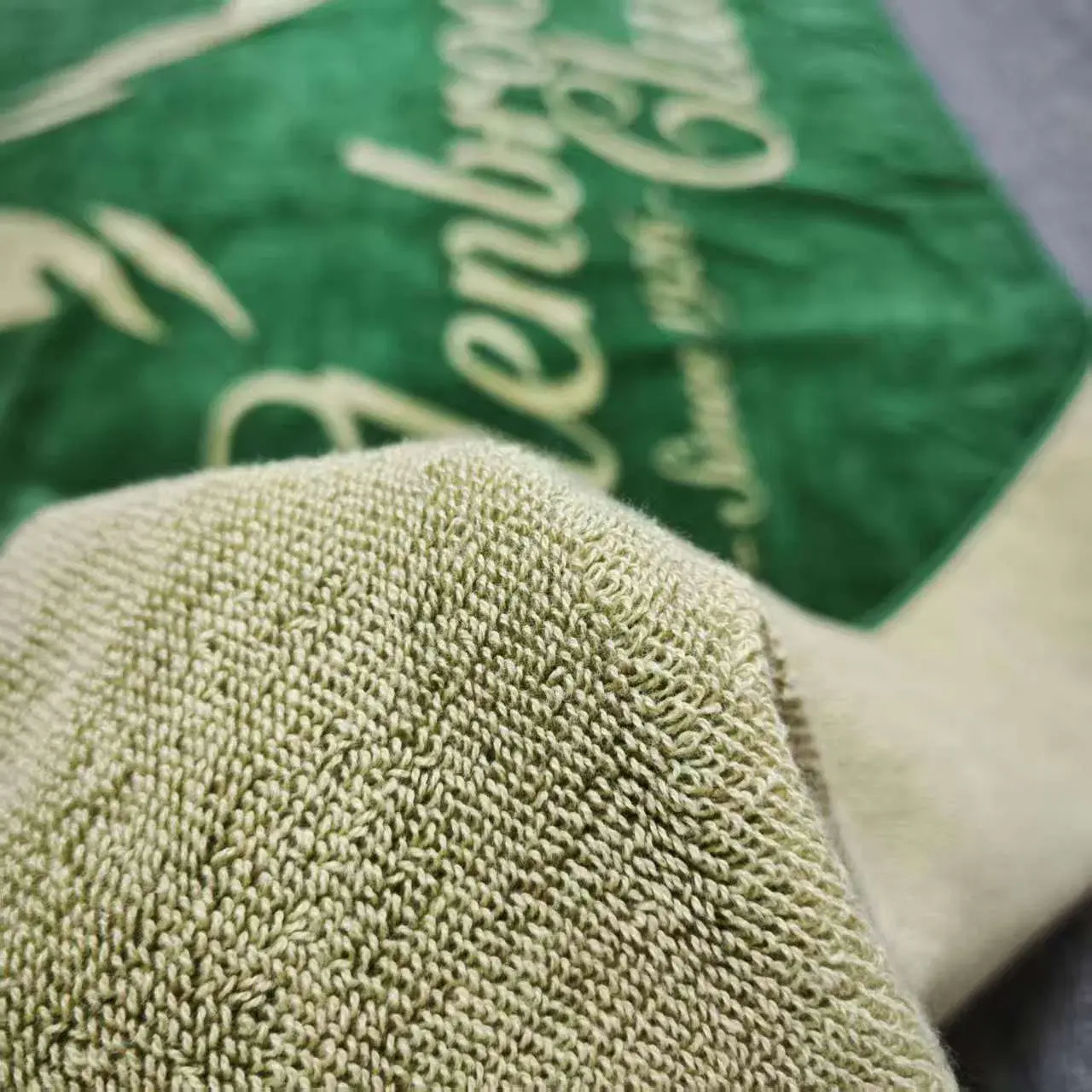 Close-up of pale looped towel texture with the green logo side visible in the background.