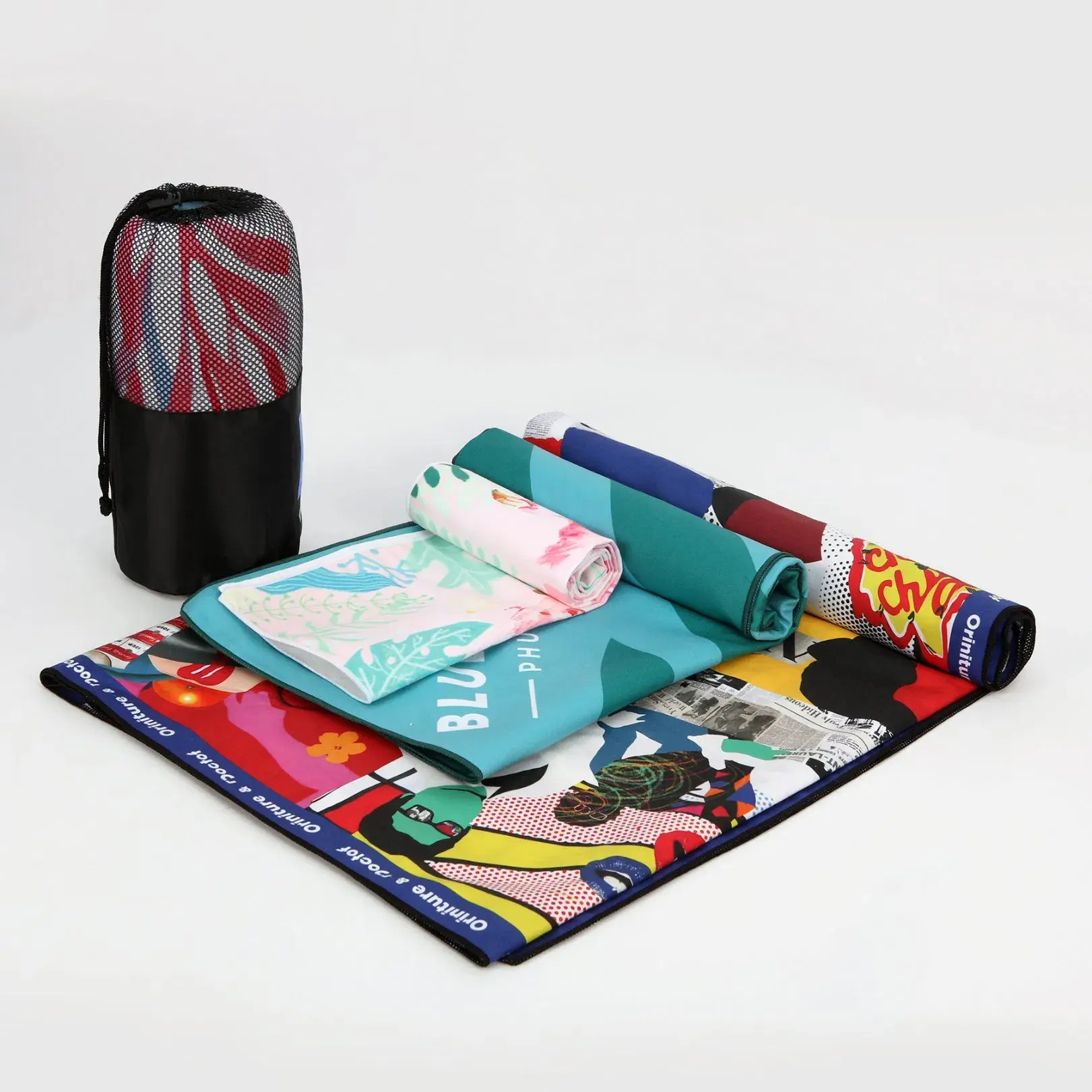 Rolled and folded beach towels with colorful prints beside a black mesh storage bag.