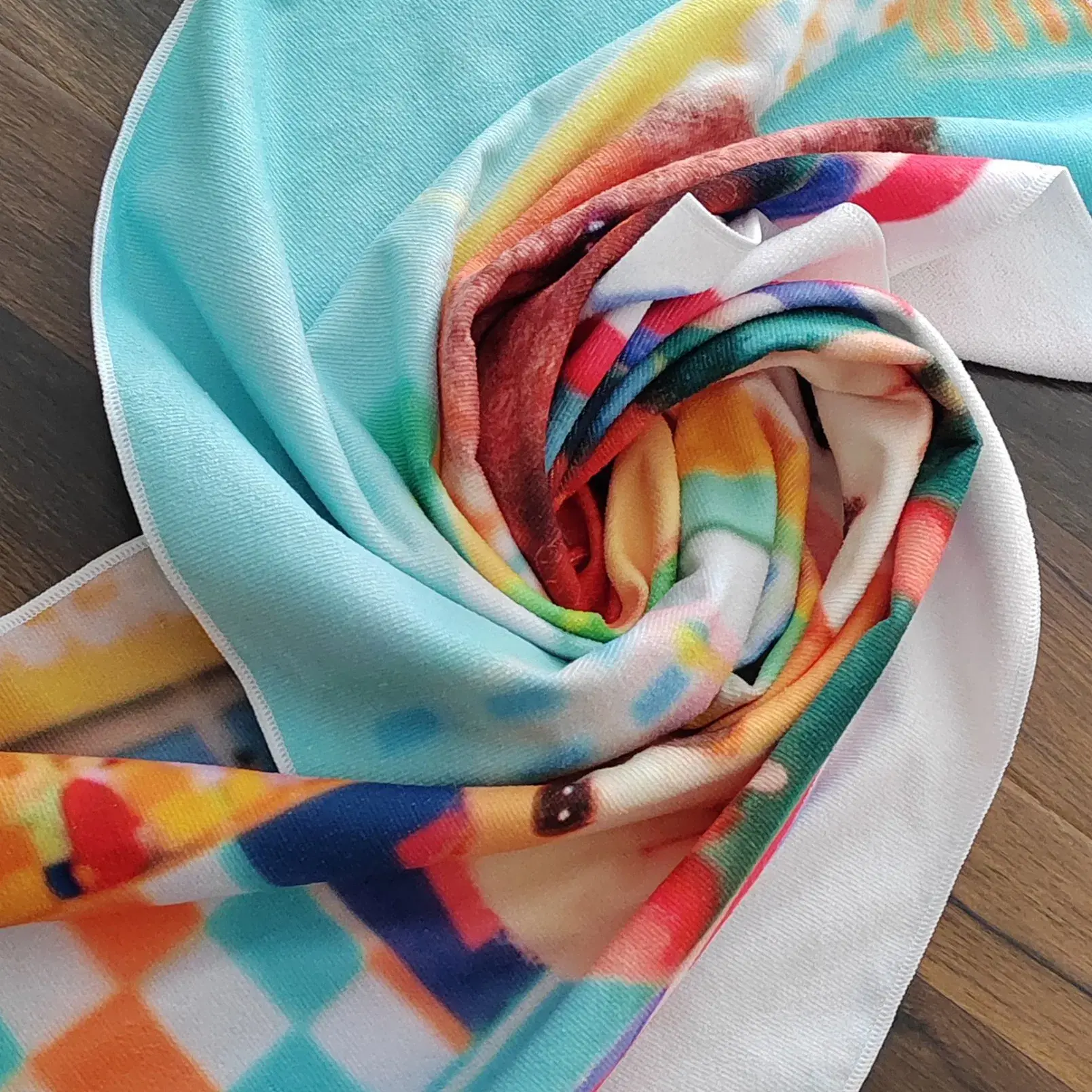 Close-up of a turquoise and multicolor printed towel showing its fabric texture and white stitched edges.