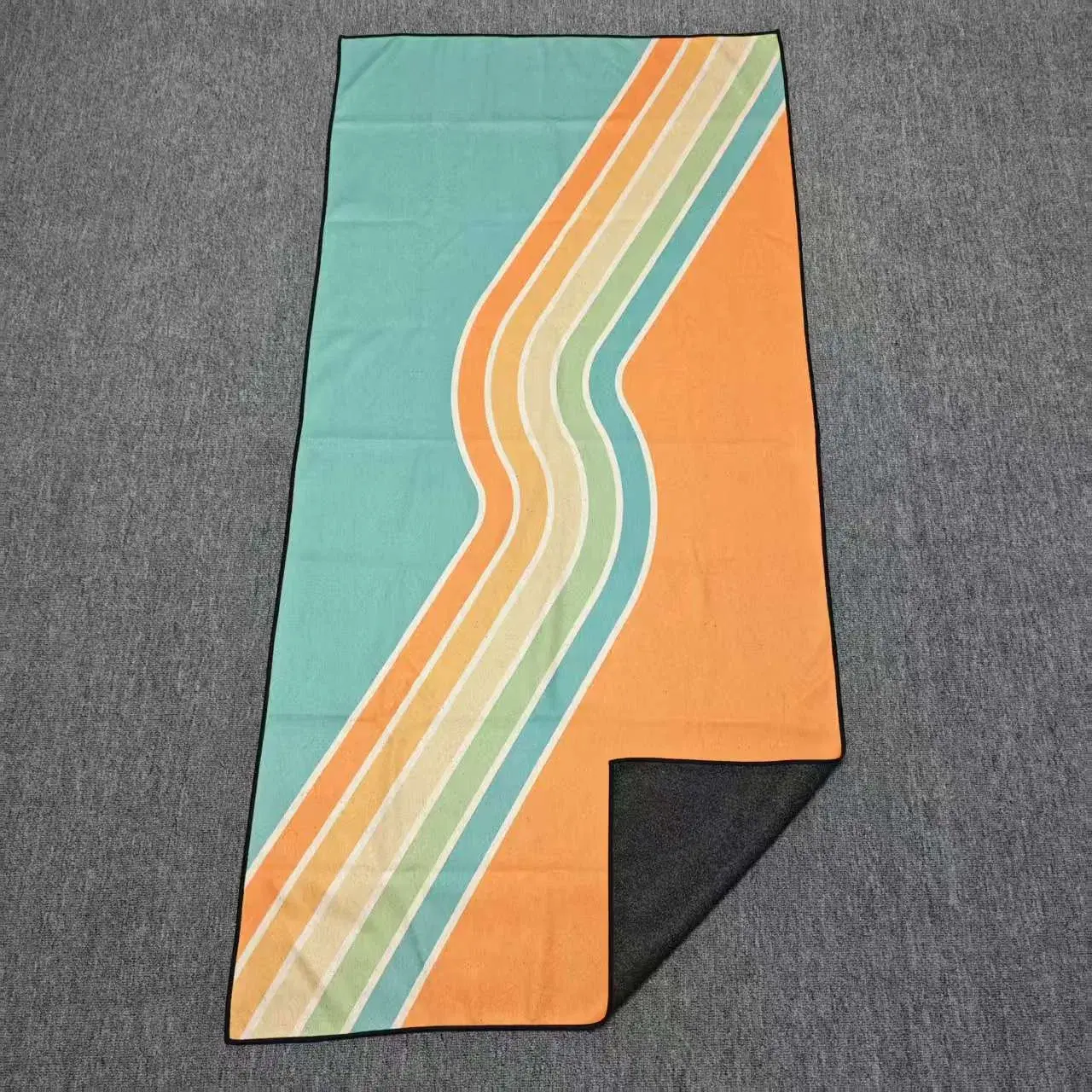 Turquoise and orange beach towel with curved pastel stripes and a folded corner showing its black reverse.