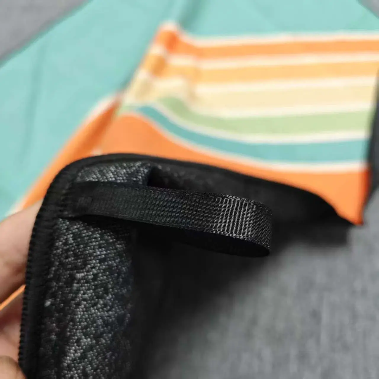 Close-up of the black reverse and hanging loop of a turquoise and orange striped beach towel.