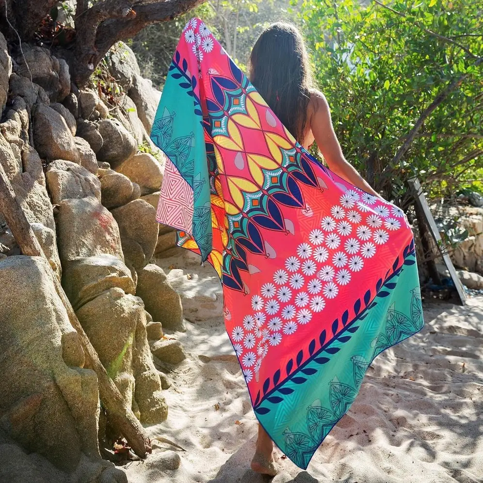 Person holding a coral pink and turquoise beach towel with white flowers, navy leaf borders and yellow geometric patterns.