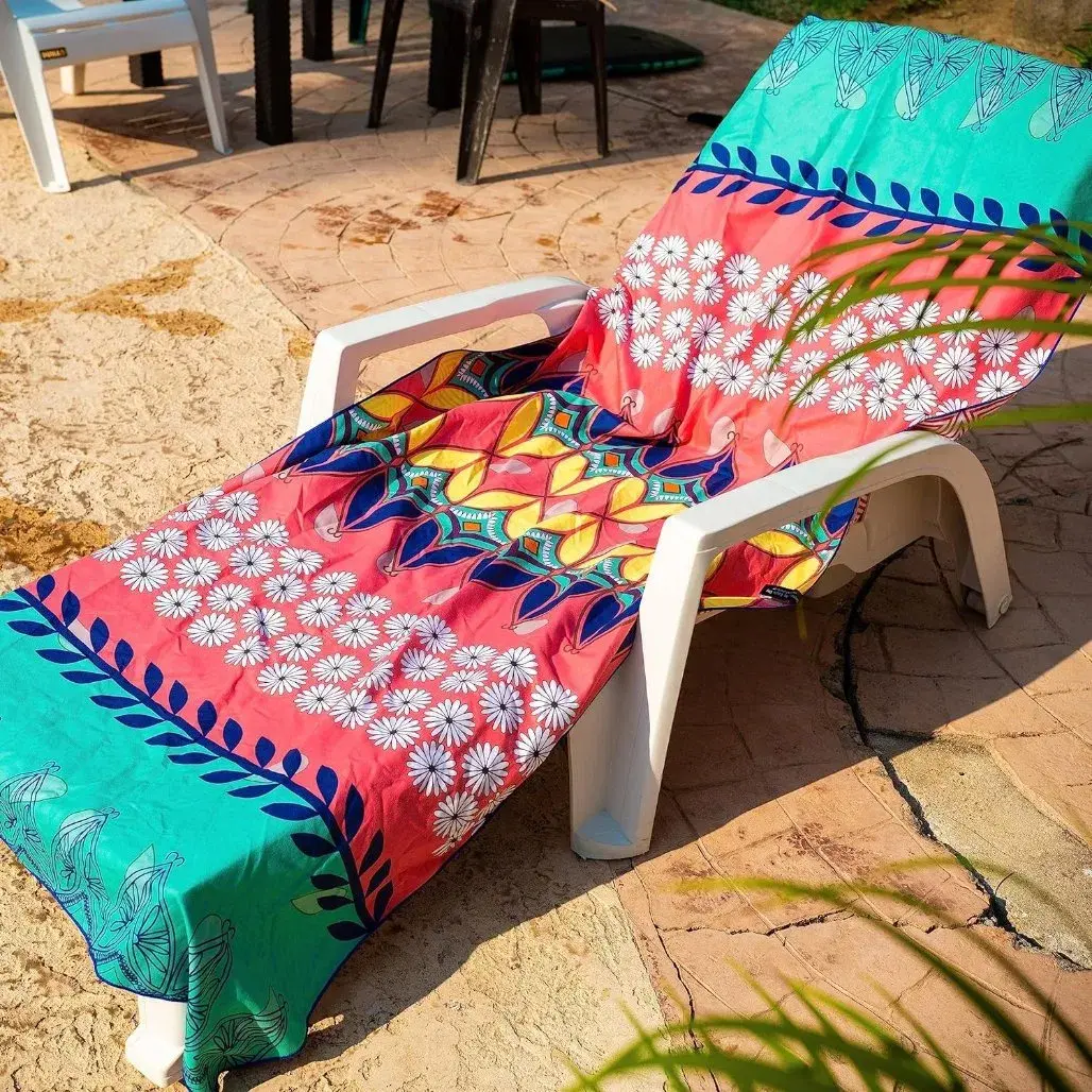 Coral pink and turquoise floral and geometric beach towel draped over a white sun lounger outdoors.