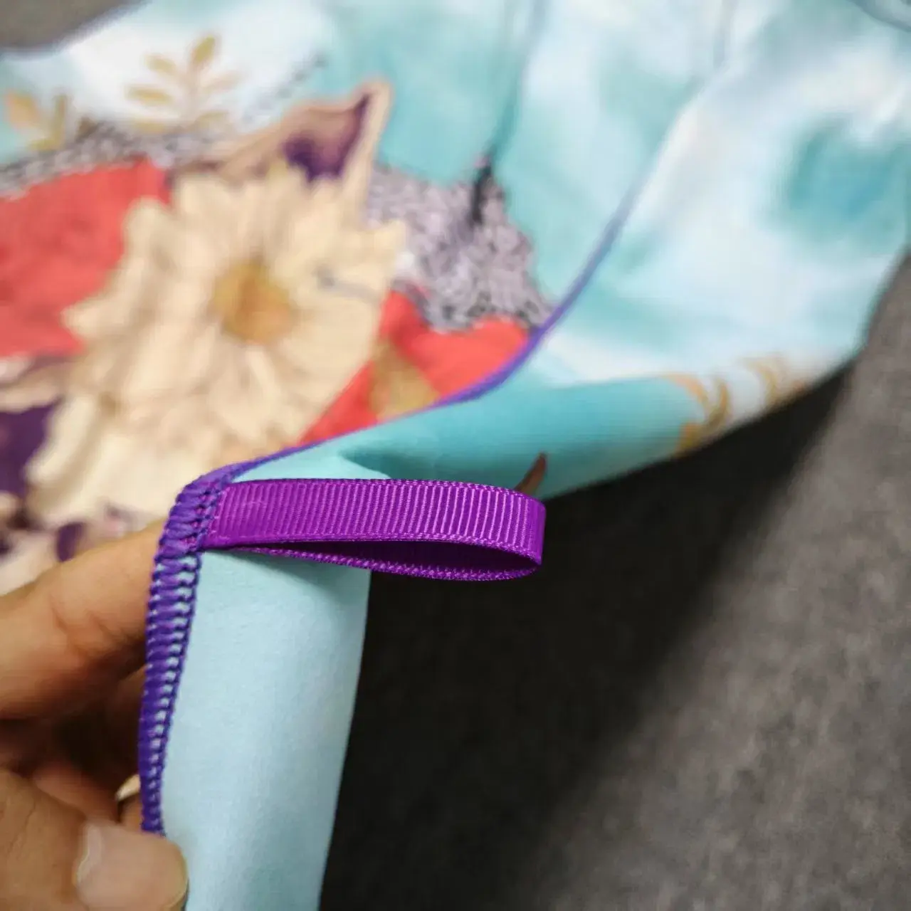 Close-up of a purple hanging loop and purple stitched edging on an aqua floral skull beach towel.