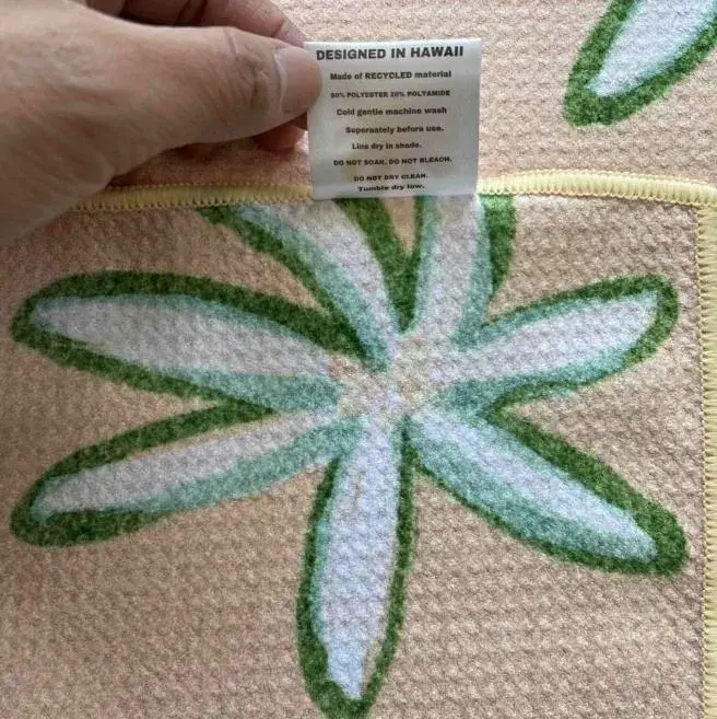 Close-up of a care label and pale yellow stitched edging on a beige towel with a green and white flower pattern.