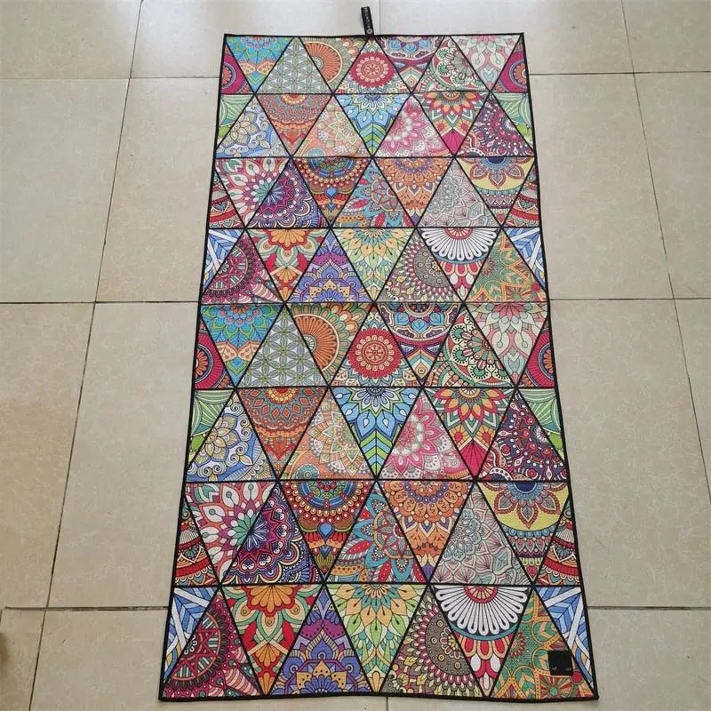 Beach towel with colorful mandala motifs in a triangular grid and black edging laid flat on a tiled floor.