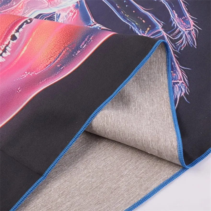 Close-up of a dark graphic-print beach towel with pink and blue details, blue stitched edging and a gray reverse.