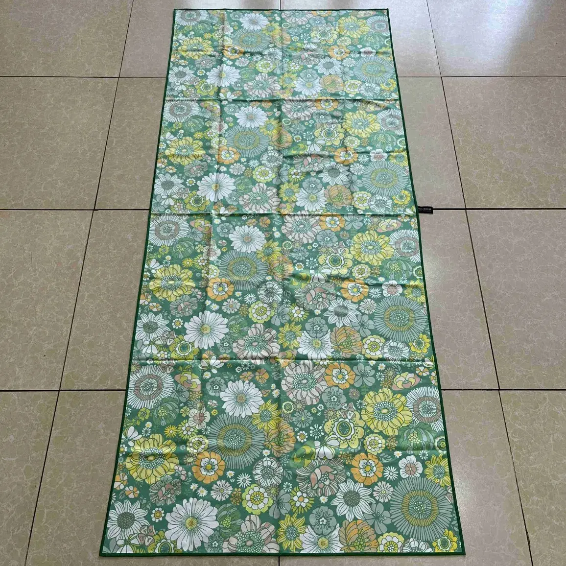 Green beach towel with white and yellow floral patterns laid flat on a tiled floor.