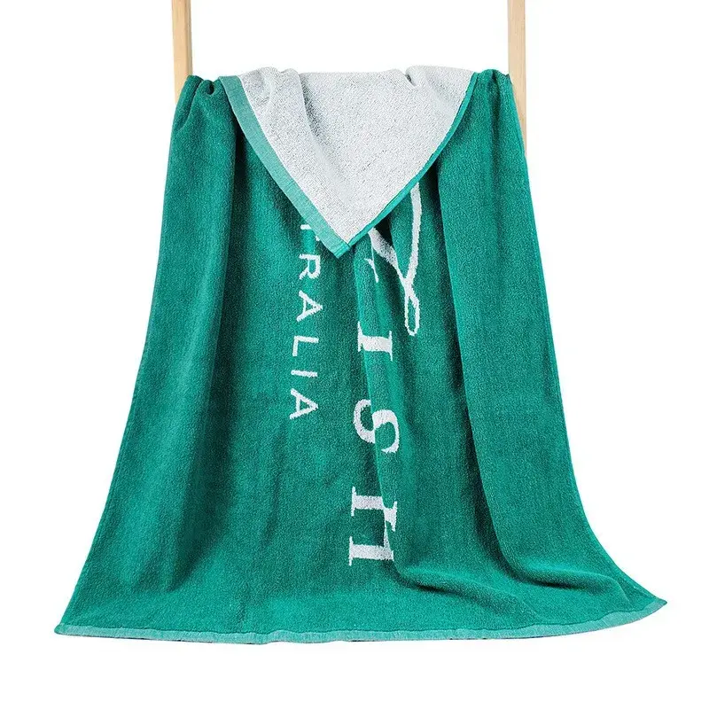 Green beach towel with white lettering draped over a wooden rack, with a folded corner showing its white reverse.