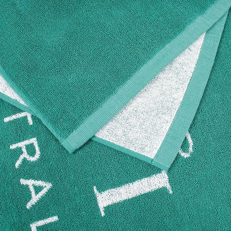 Close-up of the green towel texture and white lettering, with a folded edge showing the white reverse and green border.