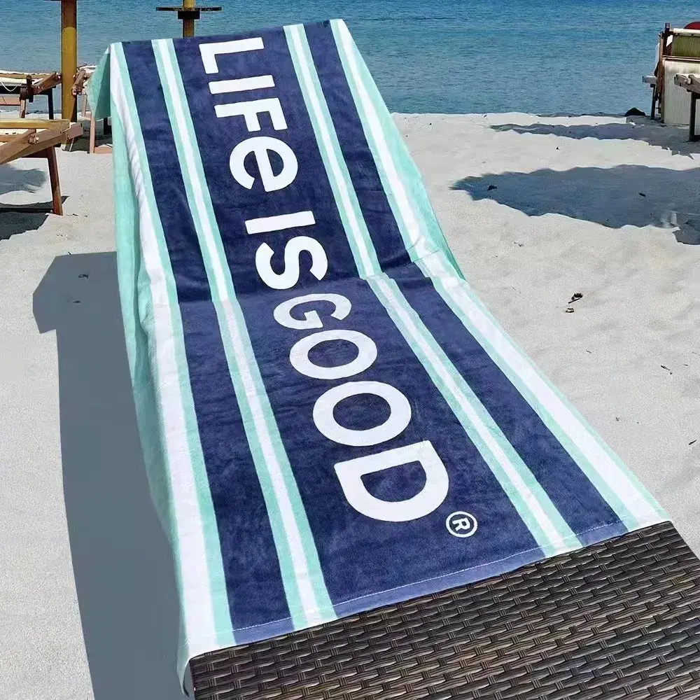 Navy beach towel with mint and white stripes and large white lettering draped over a beach lounger.