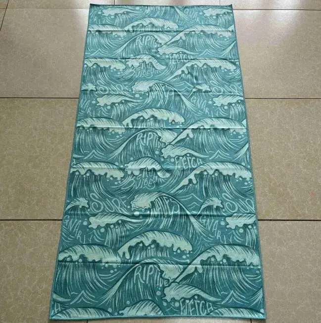 Teal beach towel laid flat with repeating curling ocean waves, pale foam and stylized lettering.