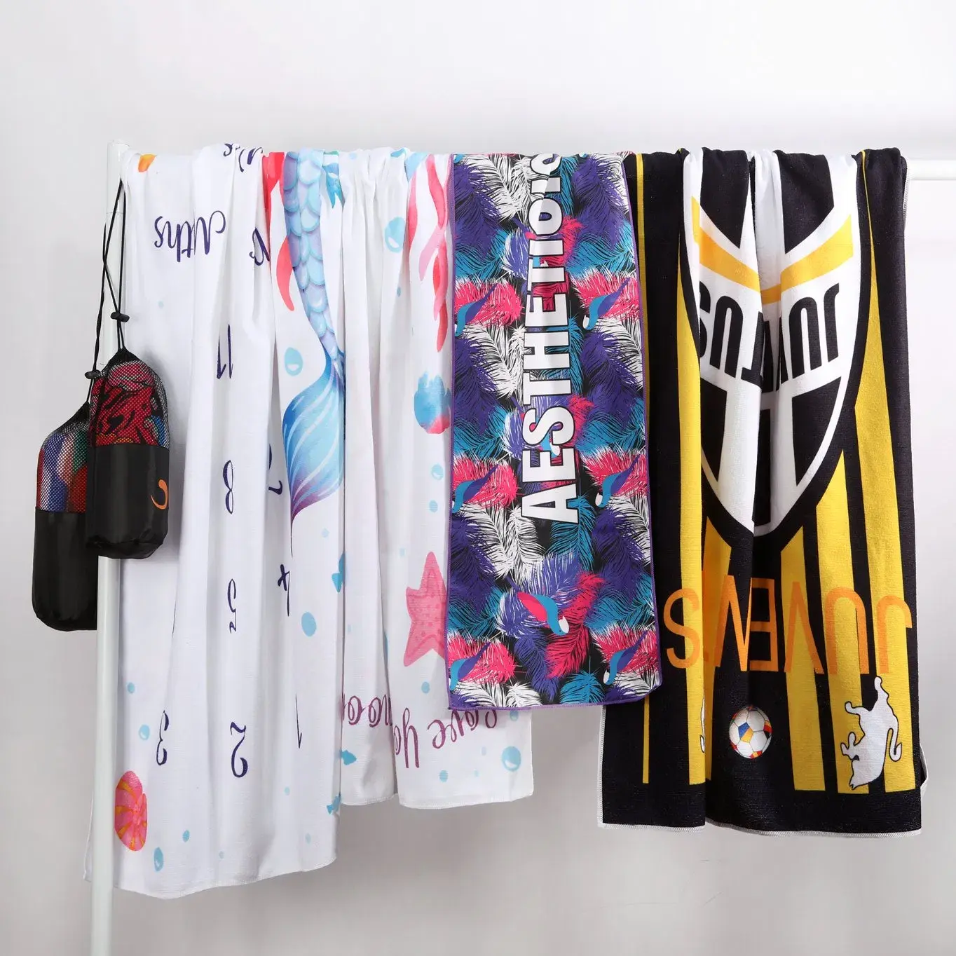 Assorted printed beach towels displayed on a rail with mesh storage bags.
