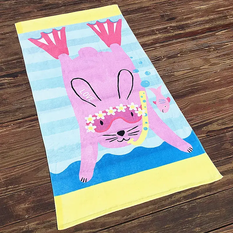 Beach towel with a pink snorkeling bunny, pale blue stripes and yellow end bands on a wooden floor.