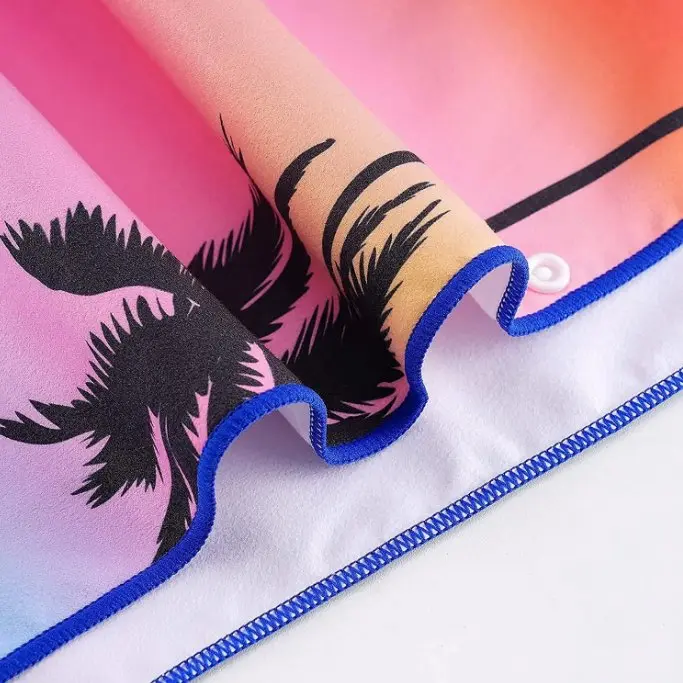 Close-up of a sunset palm-print beach towel showing blue stitched edging and a white reverse.