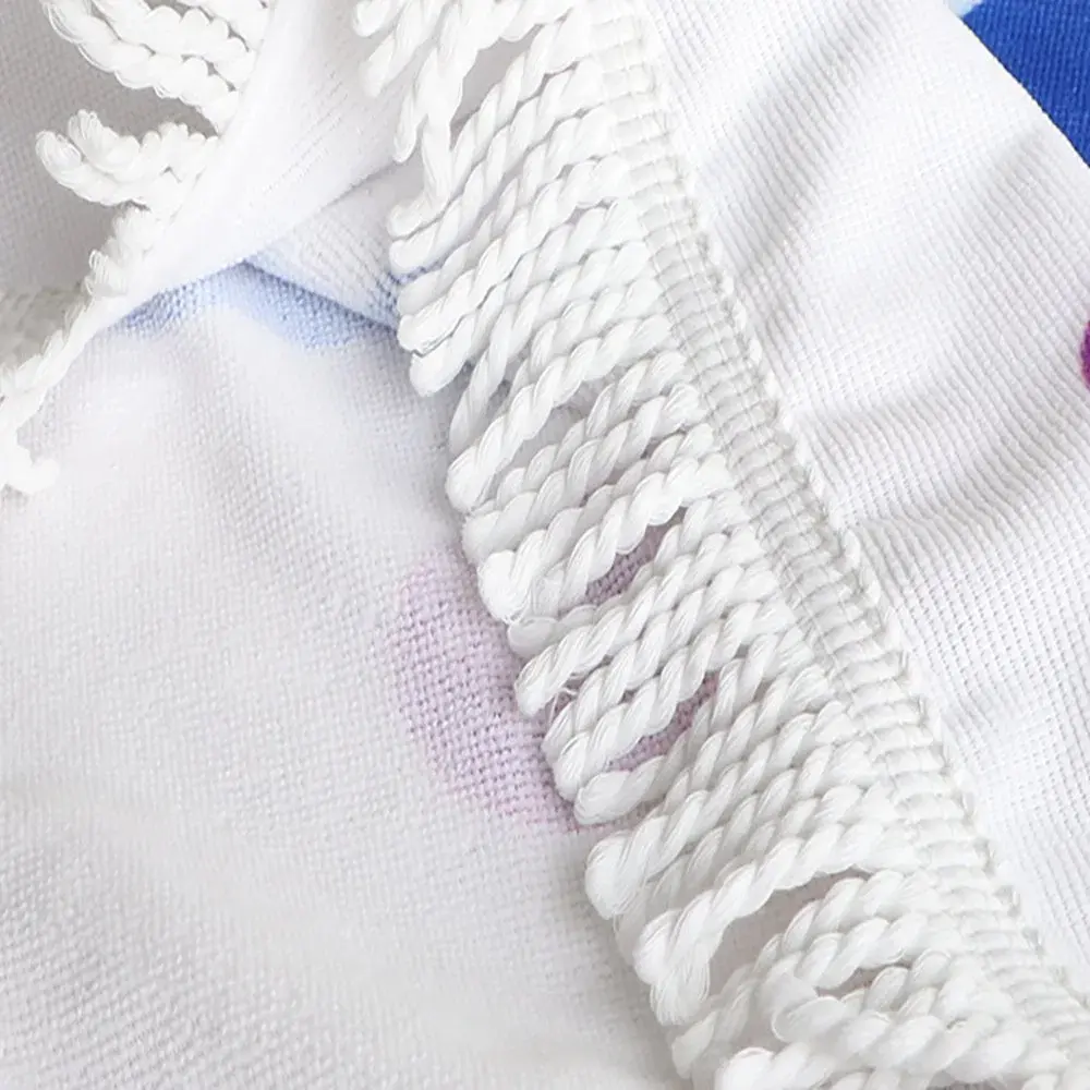Close-up of white twisted fringe, stitched edging and the textured surface of a printed round beach towel.
