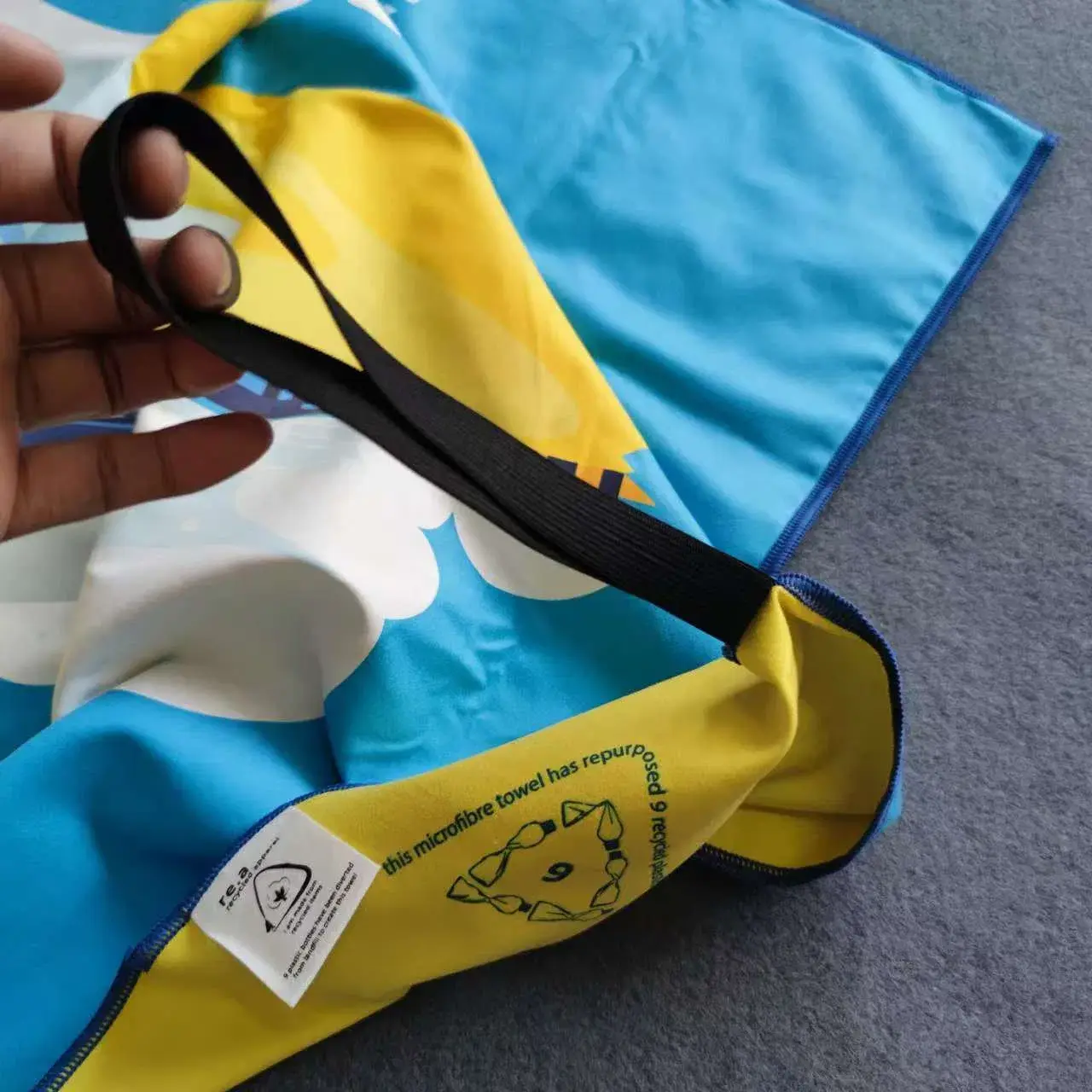 Close-up of a black hanging strap and blue stitched edging on a blue and yellow event towel.