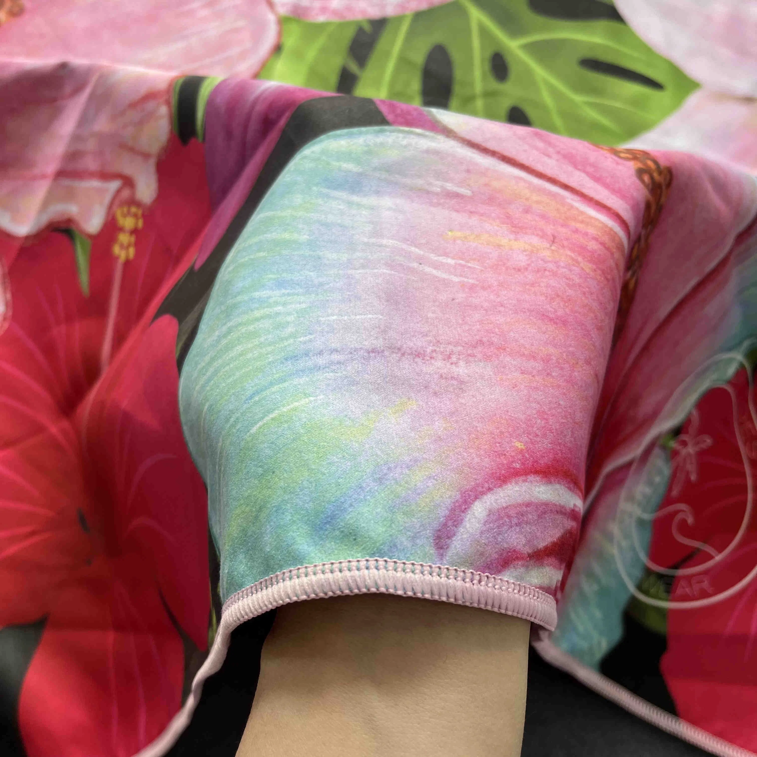 Close-up of pink floral patterns and green leaves with pale pink stitched edging on a beach towel.