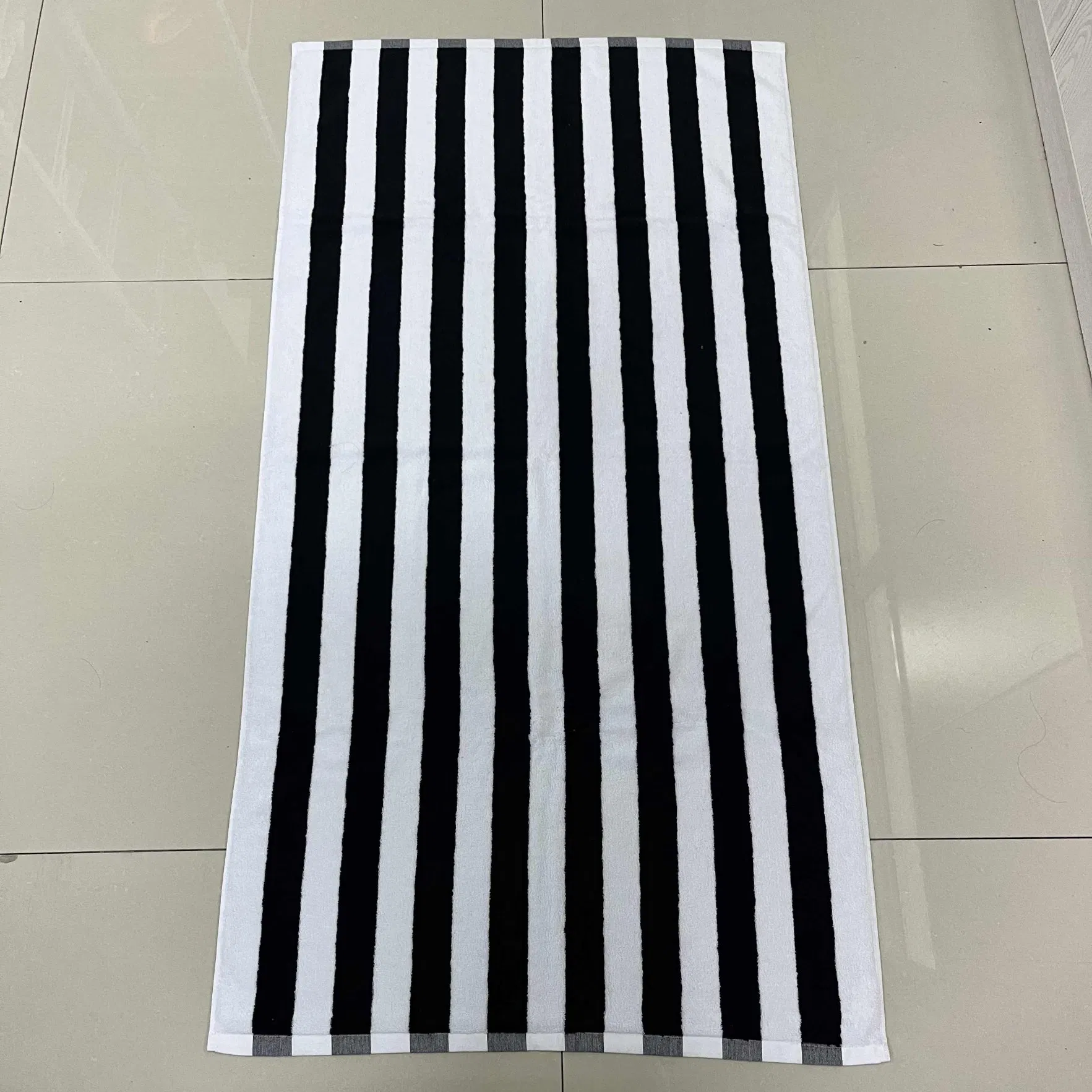 Black and white striped beach towel laid flat on a tiled floor.