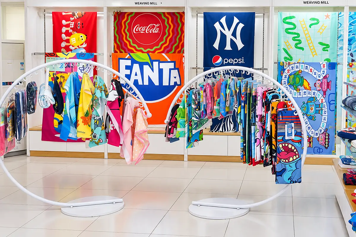 Colorful printed towels displayed on curved racks and wall panels in a towel showroom.