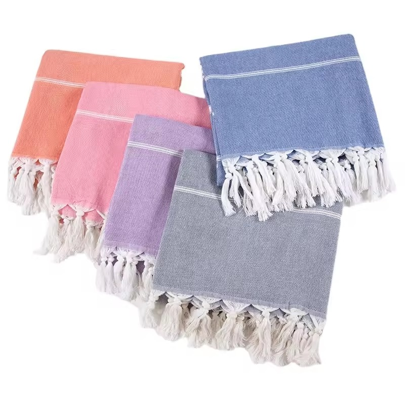 Folded Turkish beach towels in coral, pink, purple, gray and blue with white stripes and tassels.