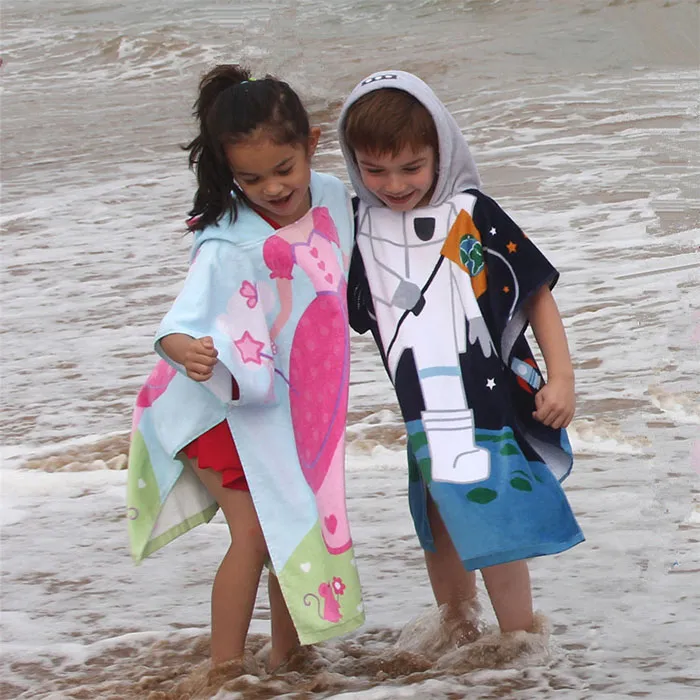 Two children wearing colorful printed hooded towels at the water’s edge.