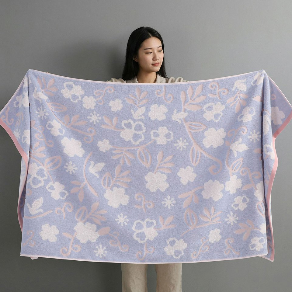 Woman holding open a lavender towel with white flowers, pink leafy stems and pink edging.